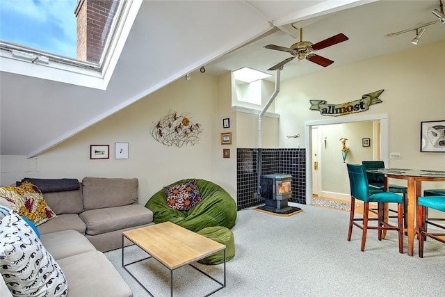 carpeted living room with vaulted ceiling with beams, ceiling fan, a wood stove, and rail lighting