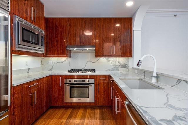 kitchen with light stone counters, stainless steel appliances, sink, and wood-type flooring