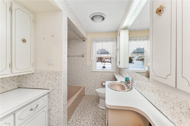 bathroom featuring vanity, tile patterned floors, toilet, a tub to relax in, and tile walls