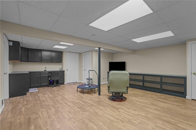 workout area with a paneled ceiling, built in desk, and light hardwood / wood-style floors