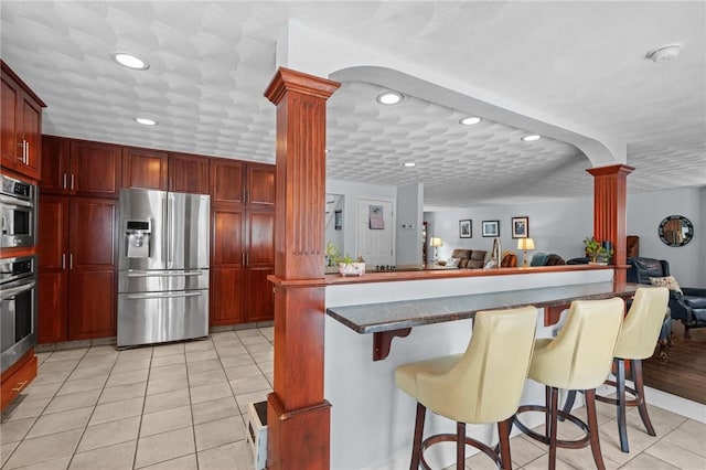 kitchen with a kitchen bar, ornate columns, light tile patterned floors, kitchen peninsula, and stainless steel appliances