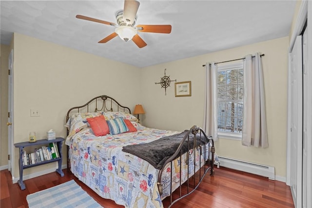 bedroom with a baseboard radiator, hardwood / wood-style floors, ceiling fan, and a closet