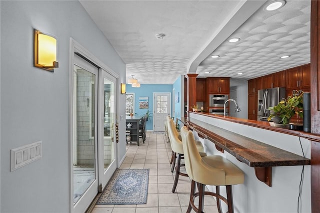 kitchen featuring sink, a breakfast bar area, appliances with stainless steel finishes, light tile patterned flooring, and kitchen peninsula