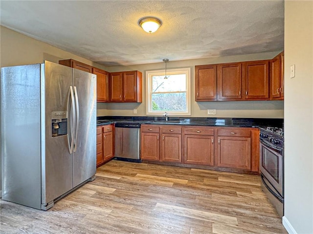 kitchen with a textured ceiling, stainless steel appliances, light hardwood / wood-style flooring, and hanging light fixtures