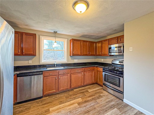 kitchen with sink, hanging light fixtures, stainless steel appliances, light hardwood / wood-style floors, and a textured ceiling