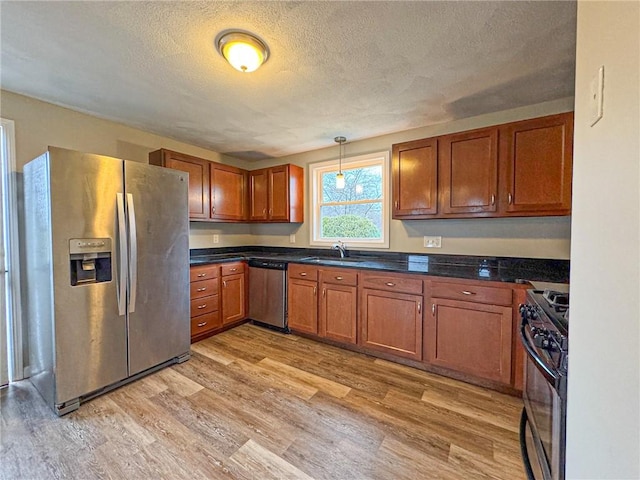 kitchen featuring sink, light wood-type flooring, a textured ceiling, appliances with stainless steel finishes, and decorative light fixtures