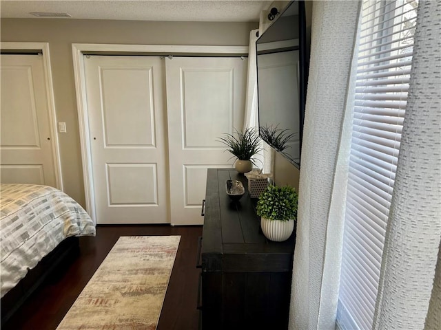 bedroom with a textured ceiling, dark wood-type flooring, and a closet