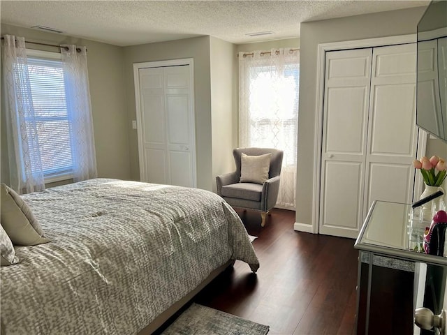 bedroom with multiple closets, dark hardwood / wood-style flooring, and a textured ceiling