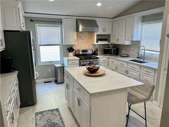 kitchen featuring stainless steel appliances, sink, wall chimney range hood, white cabinets, and a center island