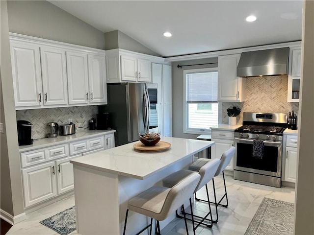 kitchen with appliances with stainless steel finishes, wall chimney exhaust hood, white cabinetry, a kitchen island, and lofted ceiling