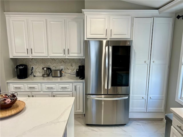 kitchen featuring backsplash, vaulted ceiling, light stone countertops, white cabinetry, and stainless steel refrigerator