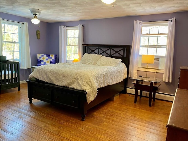 bedroom with ceiling fan, light wood-type flooring, multiple windows, and a baseboard radiator