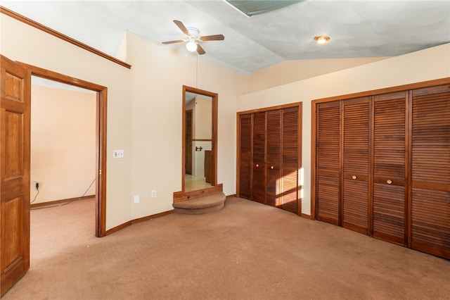 unfurnished bedroom featuring ceiling fan, two closets, light carpet, and vaulted ceiling