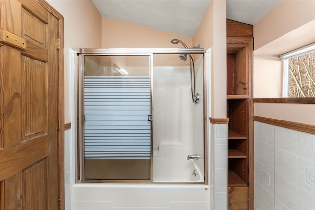 bathroom featuring tile walls, bath / shower combo with glass door, and lofted ceiling