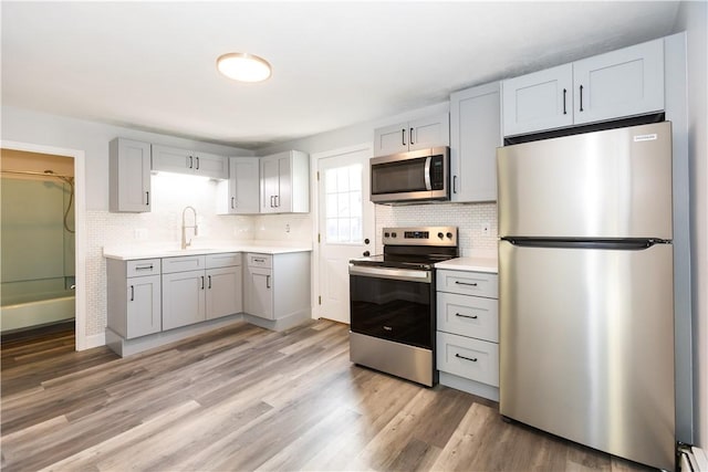 kitchen with light wood-type flooring, stainless steel appliances, gray cabinets, and sink