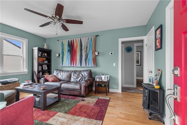 living room featuring ceiling fan, light hardwood / wood-style floors, and a wood stove