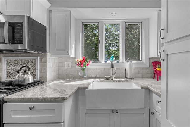 kitchen with white cabinets, sink, decorative backsplash, light stone counters, and range with gas cooktop