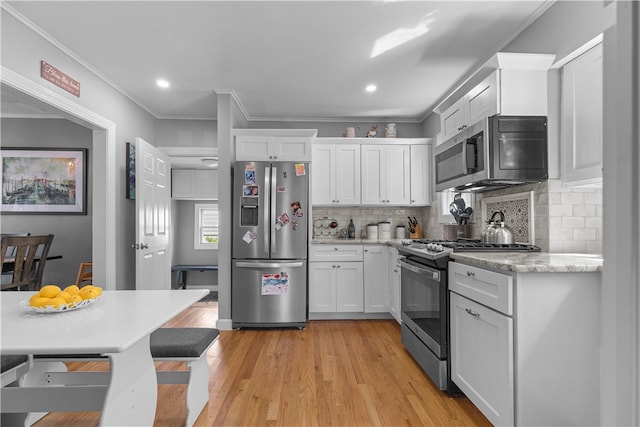 kitchen with crown molding, white cabinets, light hardwood / wood-style floors, and appliances with stainless steel finishes