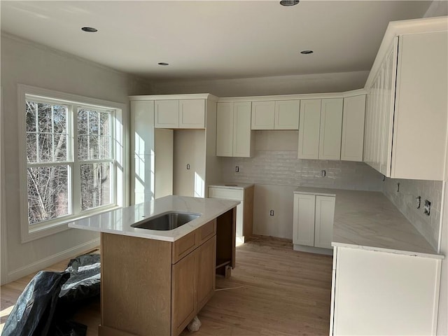 kitchen featuring backsplash, white cabinets, an island with sink, and light wood-type flooring