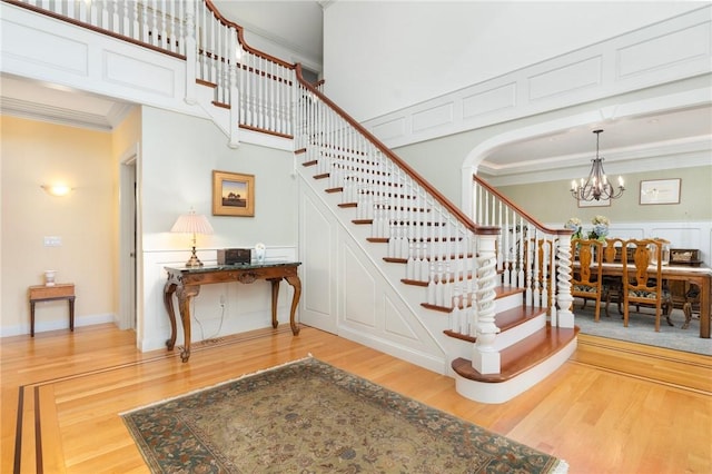 stairway with crown molding, wood-type flooring, a chandelier, and a high ceiling