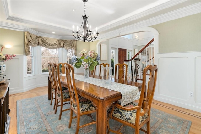 dining space with an inviting chandelier, light hardwood / wood-style floors, ornamental molding, and a raised ceiling