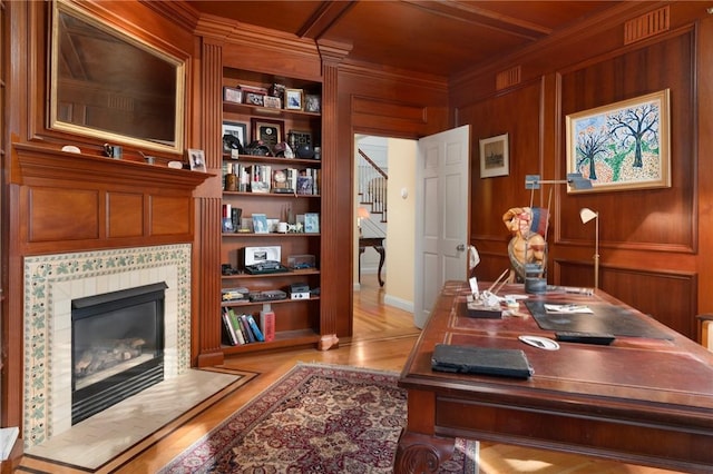 home office featuring built in features, a fireplace, wood walls, crown molding, and light hardwood / wood-style flooring