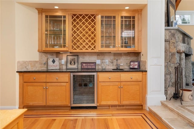 bar with dark stone countertops, beverage cooler, light hardwood / wood-style floors, and decorative backsplash