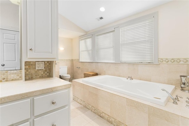 bathroom featuring lofted ceiling, tile patterned flooring, vanity, a relaxing tiled tub, and toilet