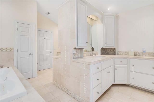 bathroom featuring lofted ceiling, vanity, tile patterned flooring, and a relaxing tiled tub