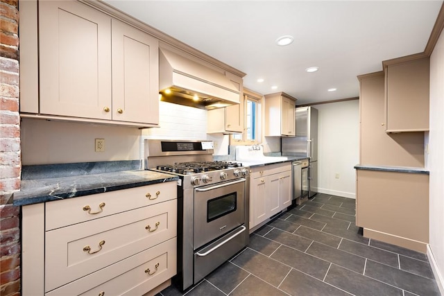 kitchen with appliances with stainless steel finishes, custom range hood, crown molding, cream cabinets, and dark stone countertops