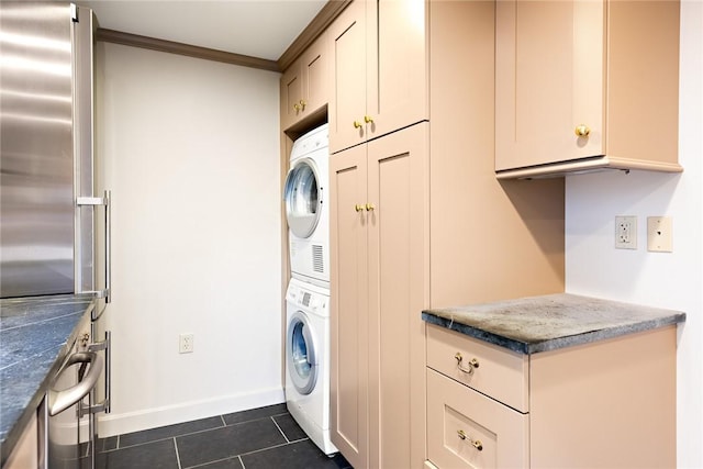 washroom with dark tile patterned flooring, ornamental molding, and stacked washer and dryer