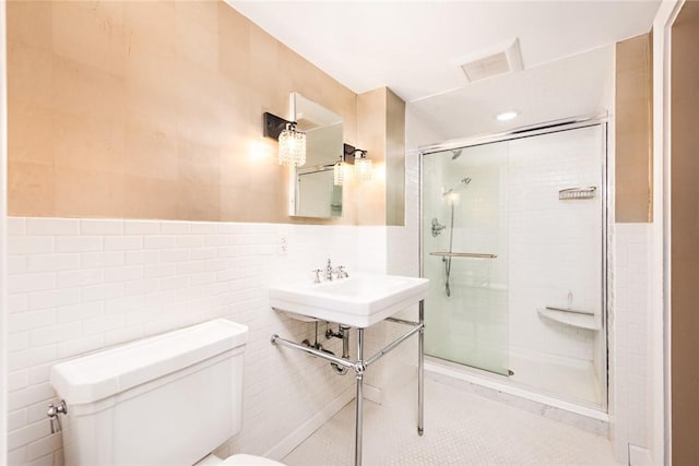 bathroom featuring sink, a shower with door, tile walls, and toilet