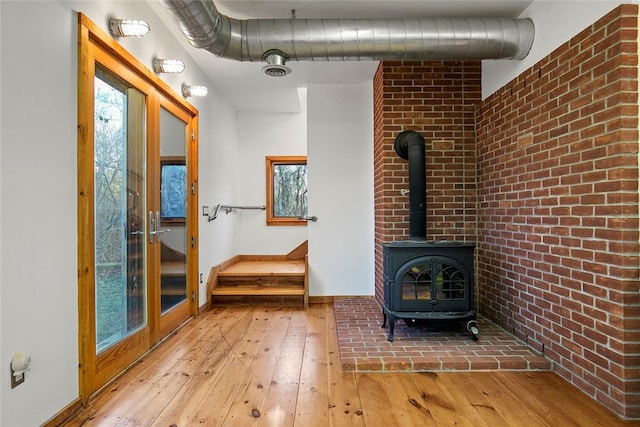 1635 Isabella Beach Rd, Southold, NY 06390 - unfurnished living room featuring hardwood / wood-style flooring, a wood stove, brick wall, and baseboards