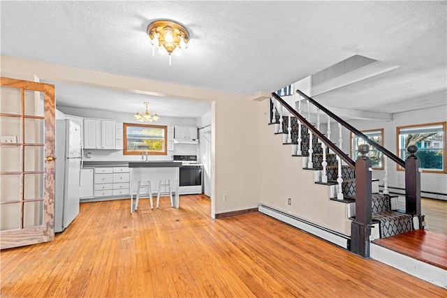 kitchen featuring a textured ceiling, white cabinets, white appliances, and a baseboard heating unit