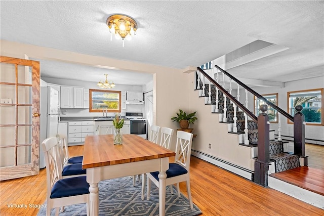 dining area with a baseboard heating unit, sink, light hardwood / wood-style flooring, a textured ceiling, and a chandelier