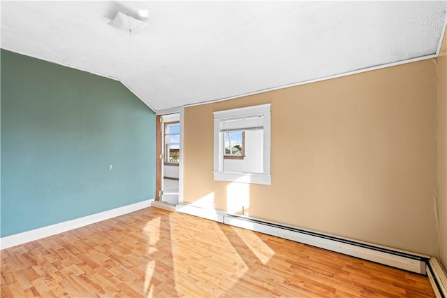 empty room featuring a baseboard heating unit, light wood-type flooring, and lofted ceiling