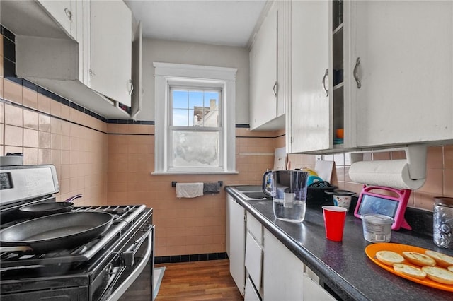 kitchen featuring white cabinets, wood-type flooring, stainless steel gas stove, and tile walls