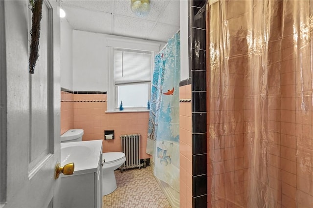 bathroom featuring a paneled ceiling, vanity, toilet, tile walls, and radiator heating unit