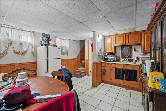 kitchen featuring a drop ceiling, sink, white fridge, wooden walls, and light tile patterned floors