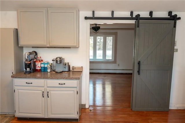 kitchen featuring a barn door, dark wood-type flooring, white cabinetry, and a baseboard heating unit