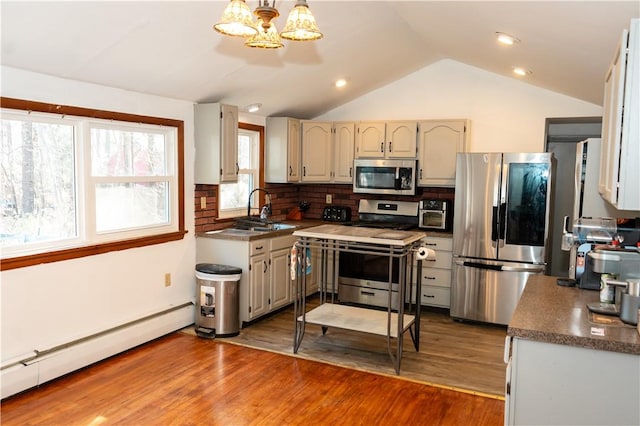 kitchen with sink, baseboard heating, vaulted ceiling, decorative backsplash, and appliances with stainless steel finishes