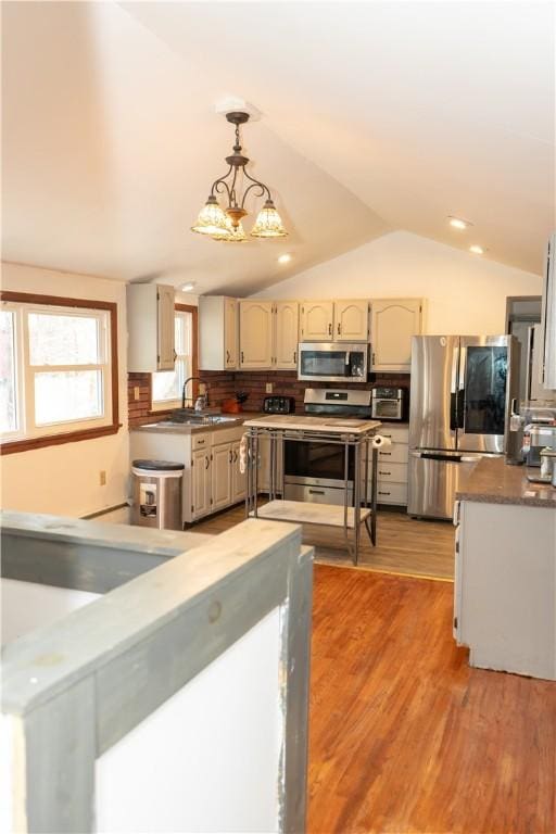 kitchen featuring pendant lighting, lofted ceiling, light wood-type flooring, appliances with stainless steel finishes, and a chandelier