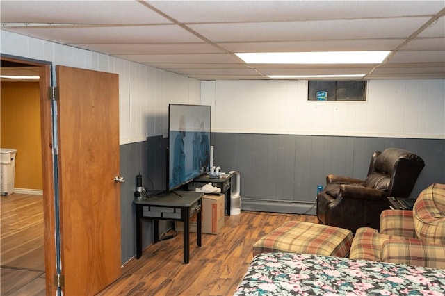 living room with hardwood / wood-style floors, a drop ceiling, wood walls, and baseboard heating