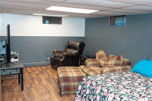 bedroom featuring hardwood / wood-style floors, a baseboard radiator, a drop ceiling, and wood walls