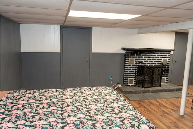 bedroom featuring a tile fireplace, a paneled ceiling, and hardwood / wood-style flooring