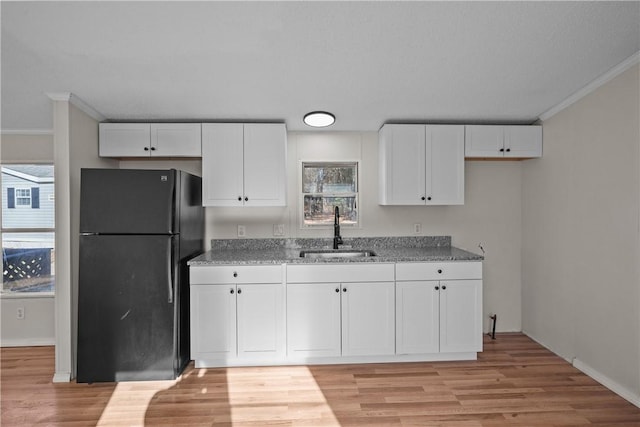 kitchen with black refrigerator, light stone countertops, white cabinetry, and sink