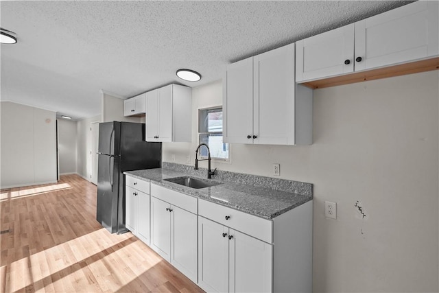 kitchen with black refrigerator, light stone counters, a textured ceiling, sink, and white cabinetry