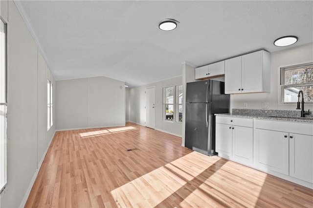 kitchen with black refrigerator, light stone countertops, light wood-type flooring, sink, and white cabinetry