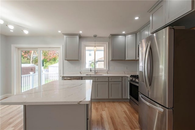 kitchen with pendant lighting, stainless steel appliances, sink, gray cabinets, and light wood-type flooring