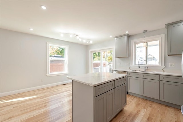 kitchen featuring gray cabinets, a kitchen island, light hardwood / wood-style floors, sink, and light stone counters